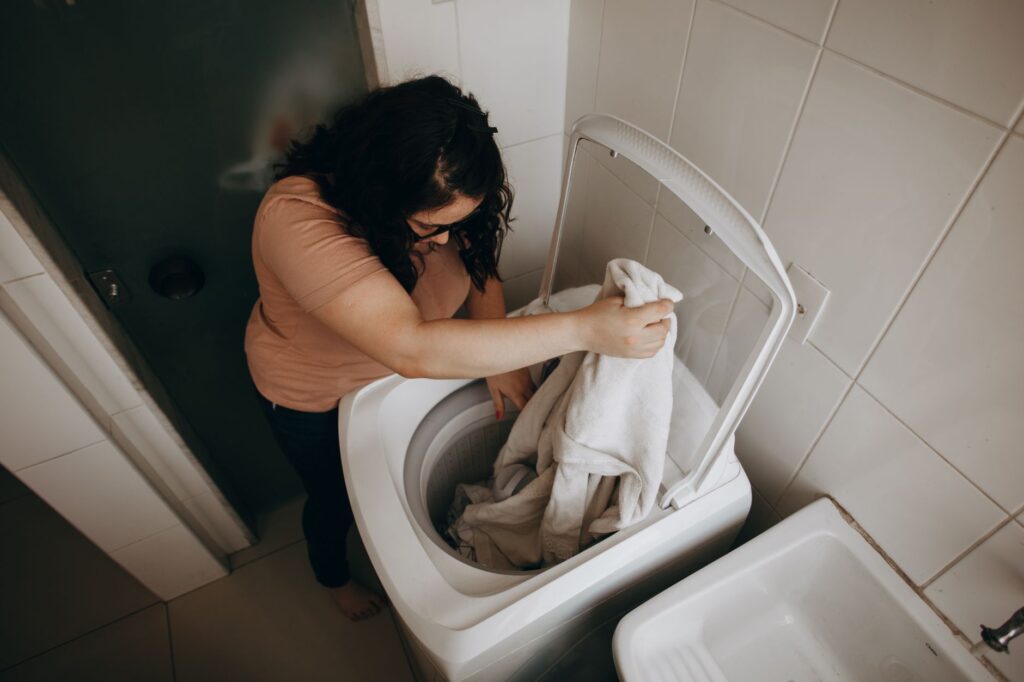 Woman loading laundry into a top-load washing machine from above, lid open - Maytag washer troubleshooting guide