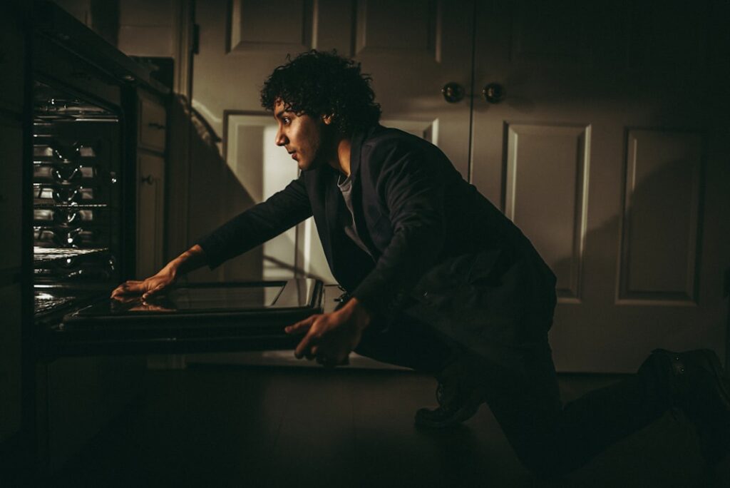 Homeowner crouching down to inspect an open oven, troubleshooting a heating problem